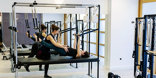 Mujer realizando ejercicios en una máquina cadillac V2 con ayuda de una monitora en una sala de Esencia Pilates. Clases de pilates en Villa del Prado Valladolid