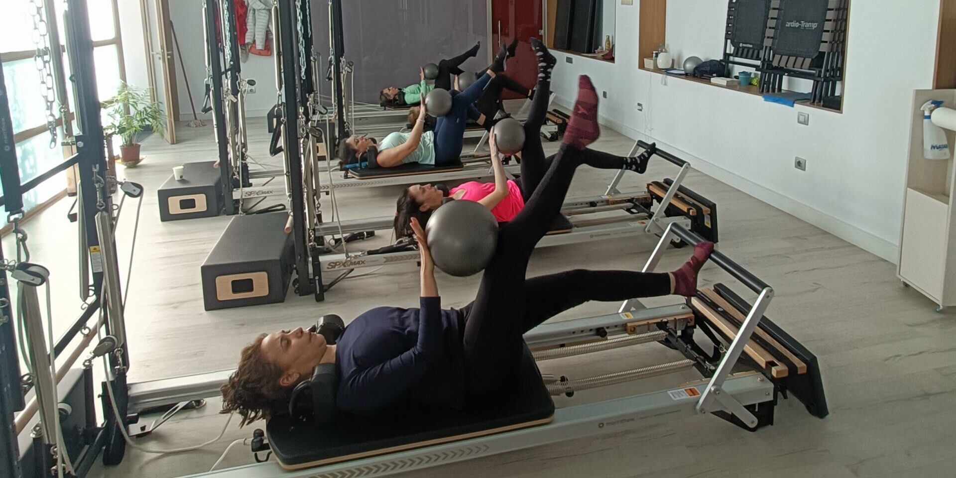 Dos alumnos practicando stability chair frente a una monitora en una sala de Esencia Pilates